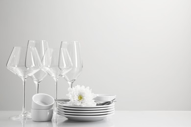 Photo of Set of many clean dishware, cutlery, glasses and flower on light table. Space for text