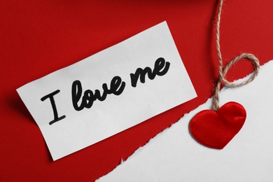 Paper with handwritten phrase I Love Me and heart on red background