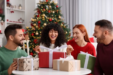 Photo of Christmas celebration in circle of friends. Happy woman opening gift at home