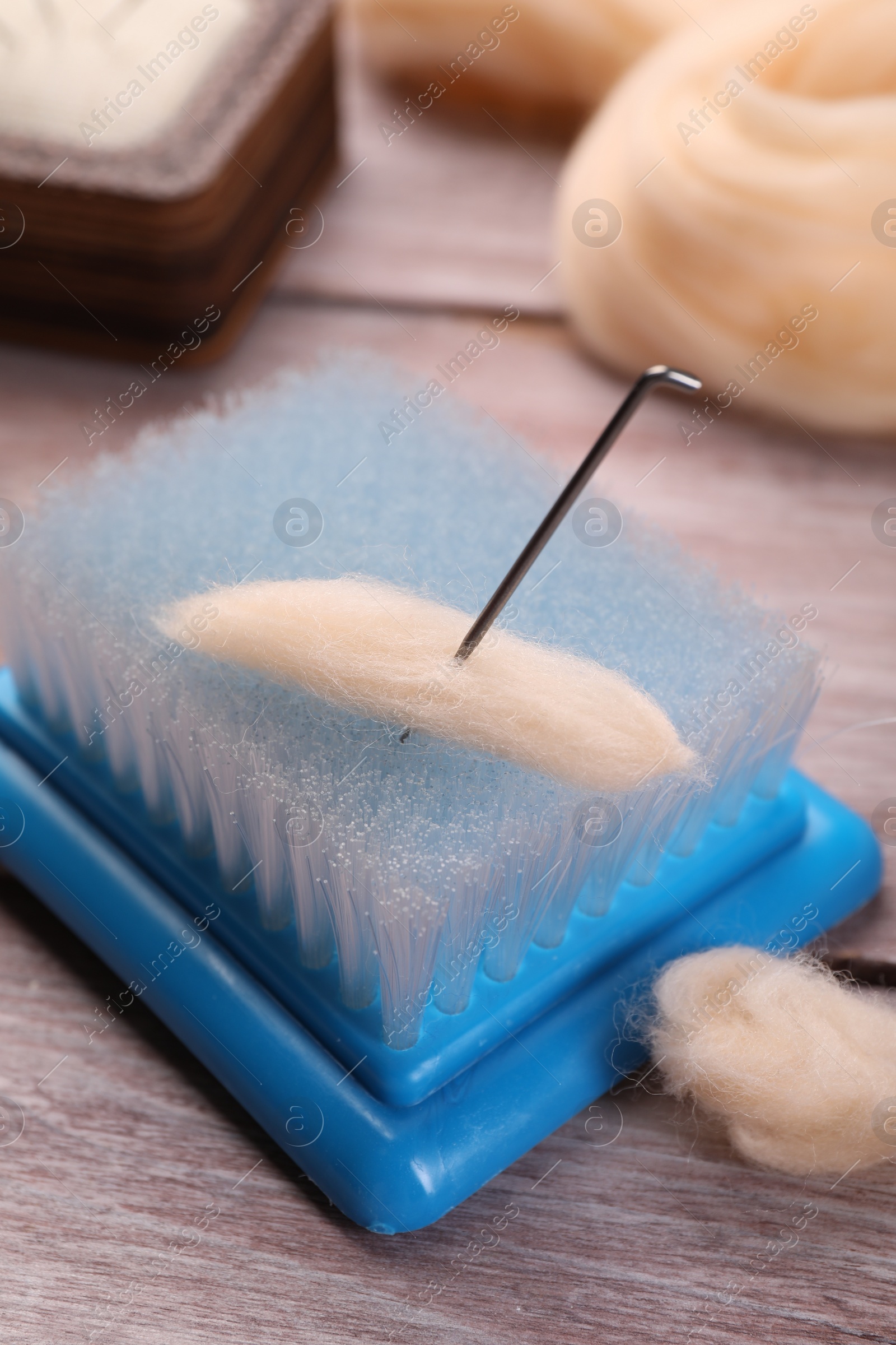 Photo of Felting wool, brush and needle on wooden table, closeup