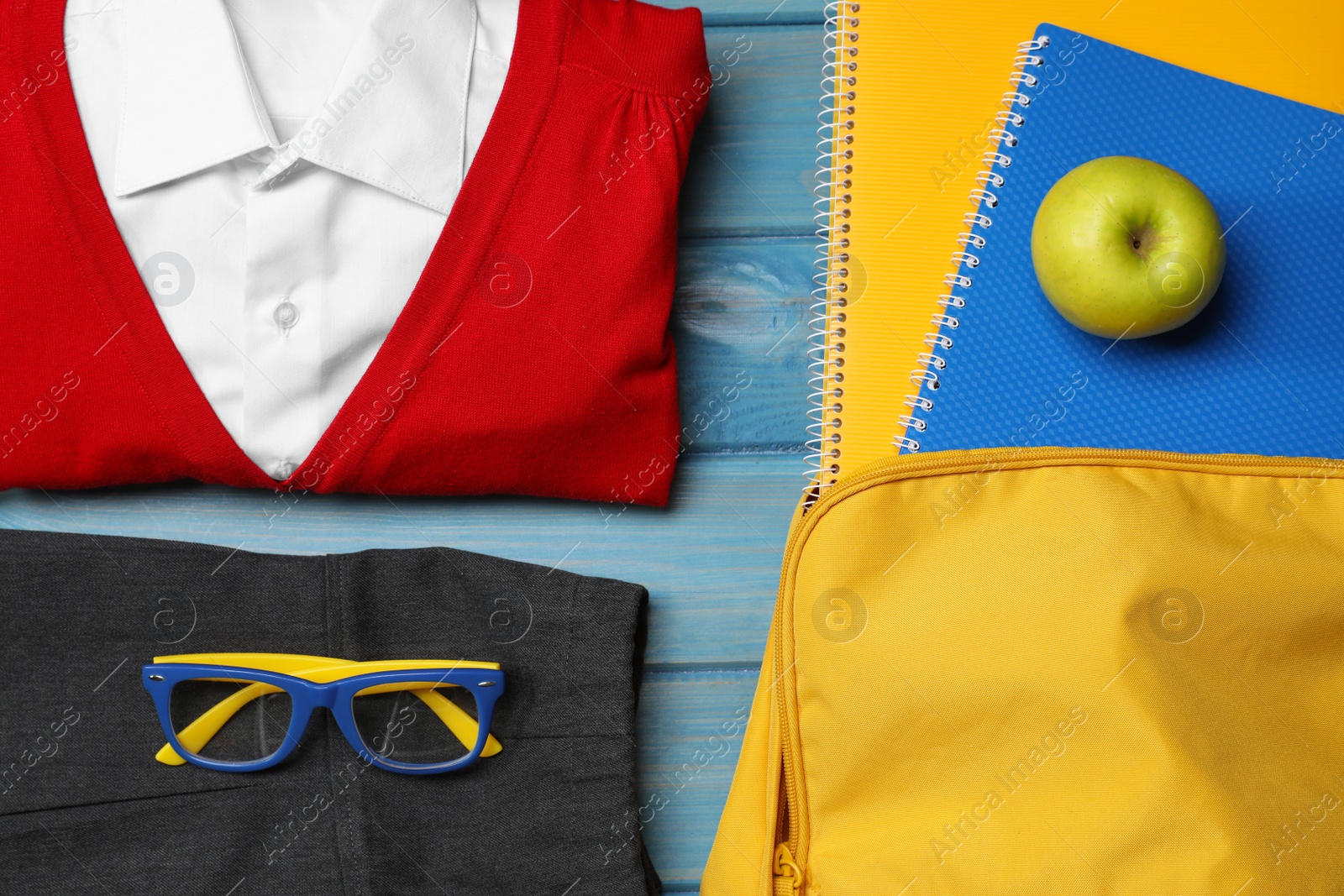 Photo of Stylish school uniform for girl, backpack with notebooks and apple on light blue wooden background, flat lay