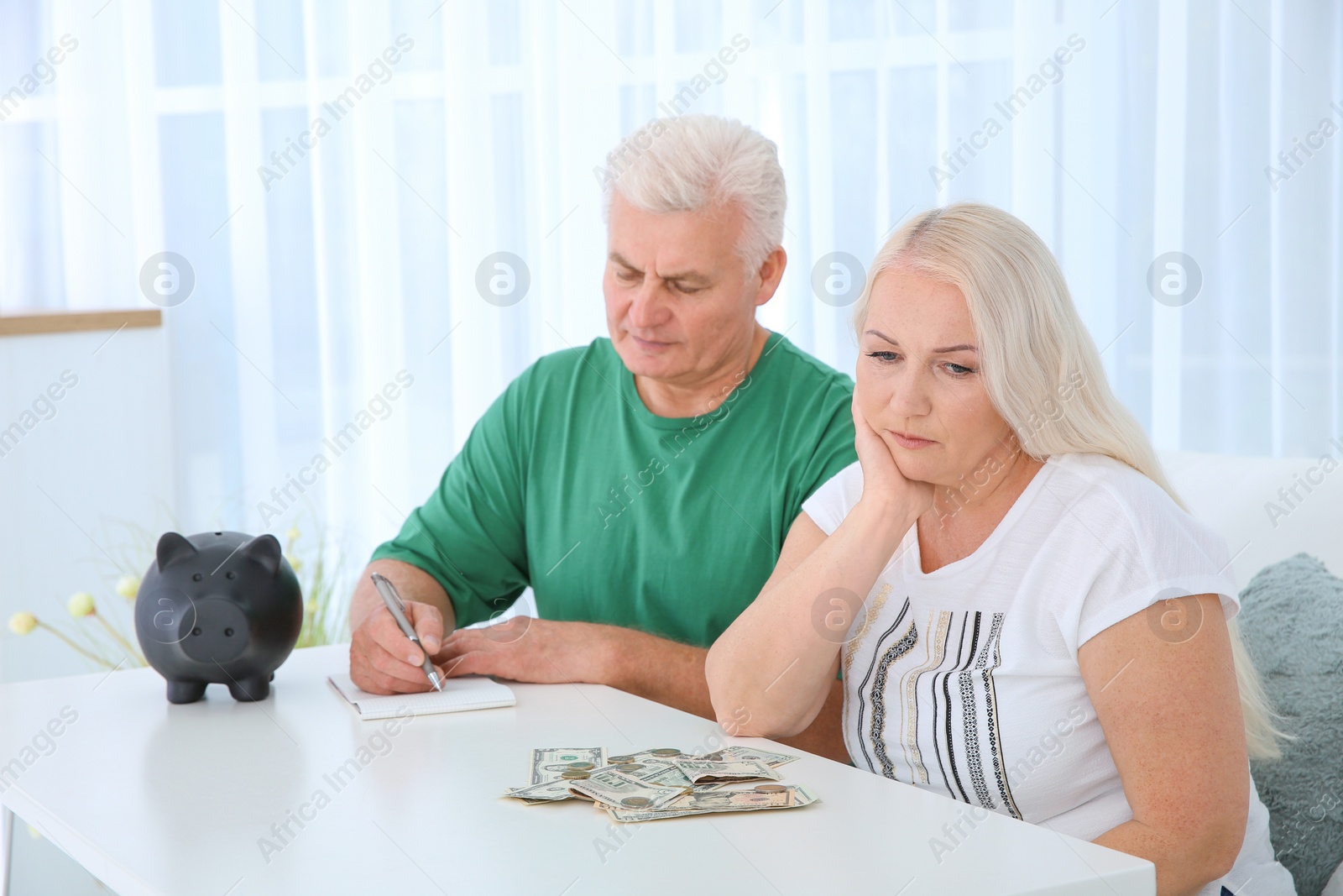 Photo of Mature couple with money and piggy bank at table