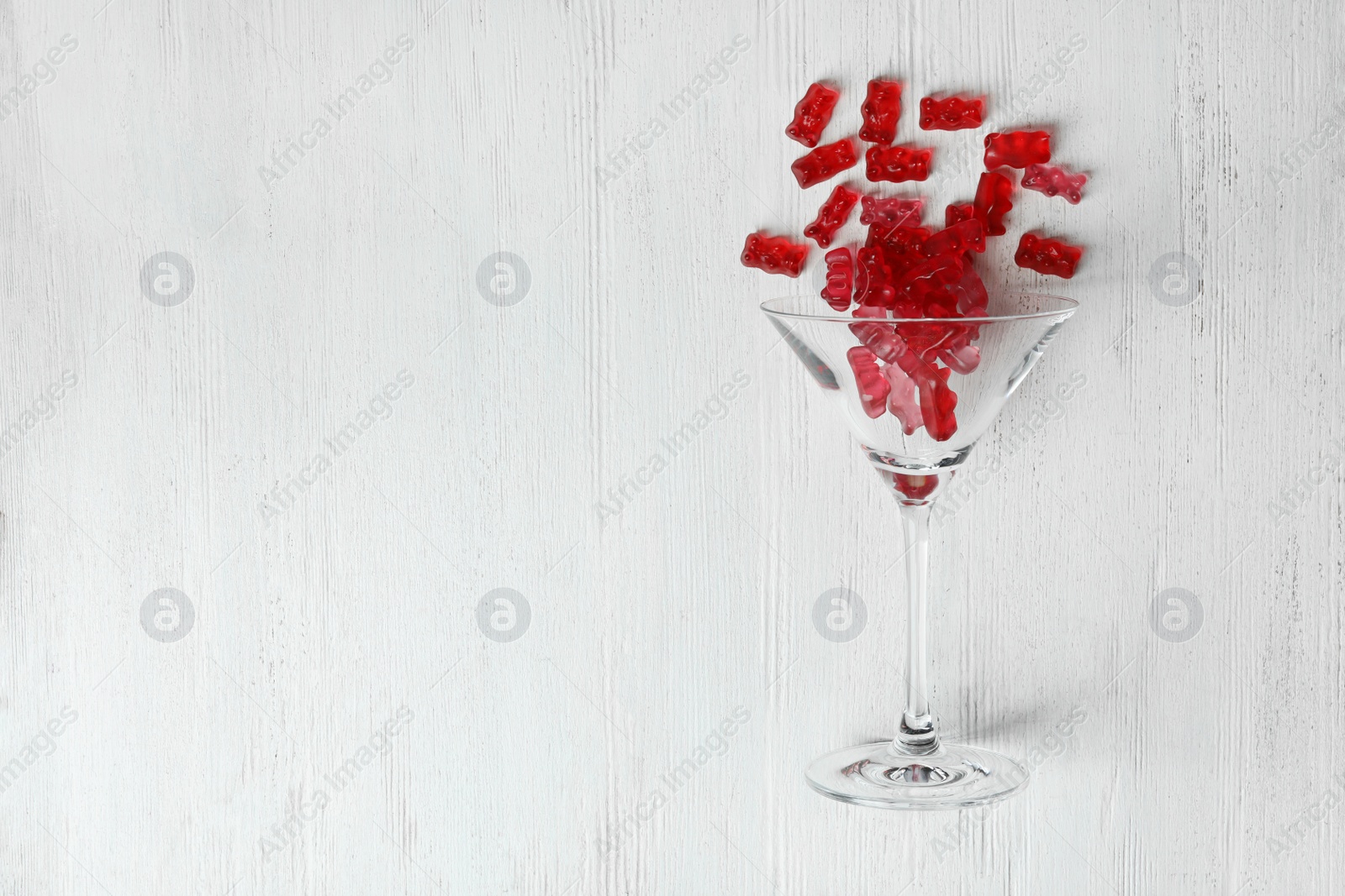 Photo of Martini glass with delicious jelly bears on wooden background, top view. Space for text