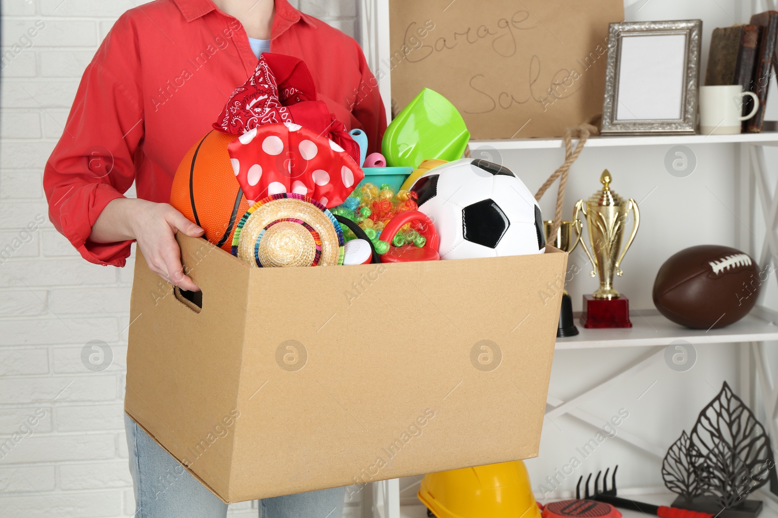 Photo of Woman holding box of unwanted stuff indoors, closeup