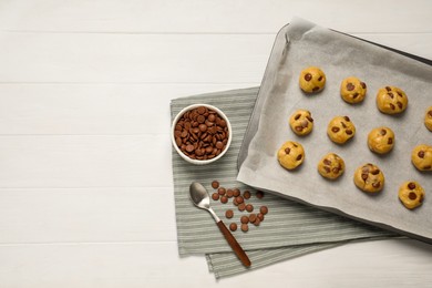 Baking pan with unbaked cookies and chocolate chips on white wooden table, flat lay. Space for text