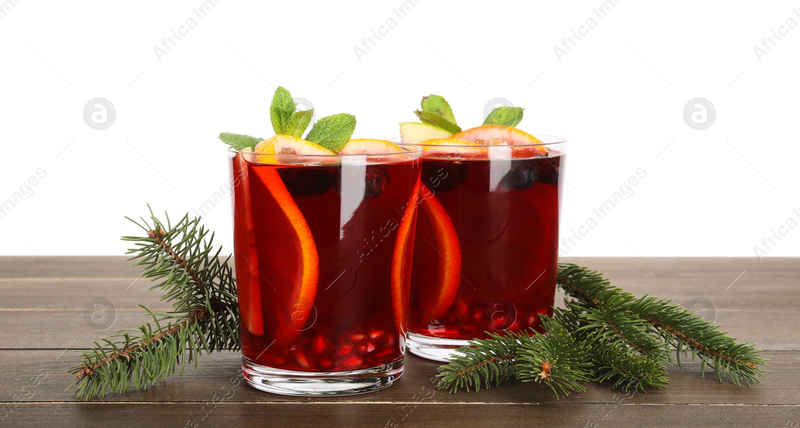Photo of Aromatic Christmas Sangria drink in glasses and fir branches on wooden table against white background