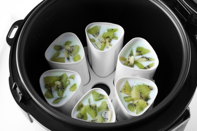 Cups of homemade kiwi yogurt in modern multi cooker on white background