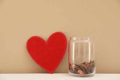 Photo of Red heart and donation jar with coins on table against color background