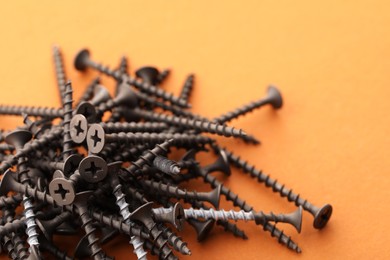 Many metal screws on orange background, closeup