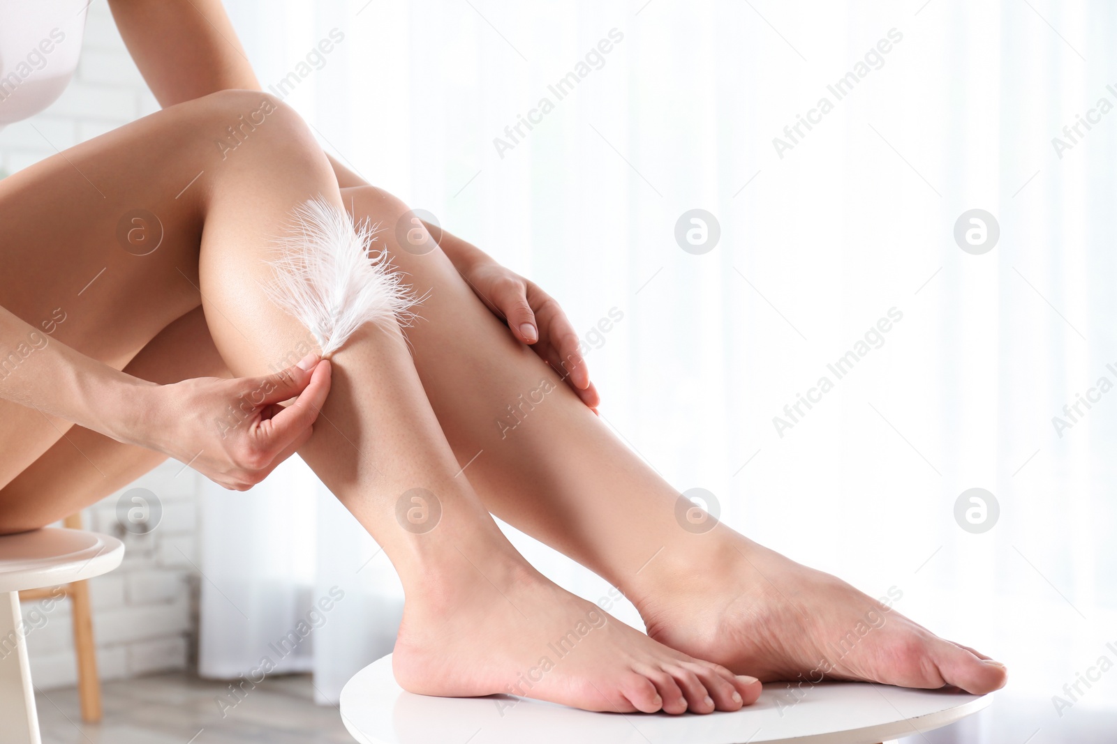 Photo of Woman touching leg with feather indoors, closeup. Epilation procedure