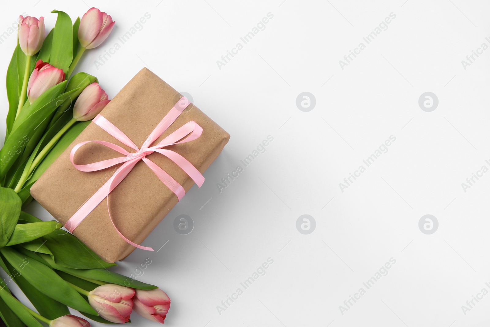 Photo of Beautiful gift box with bow and pink tulips on white background, flat lay. Space for text