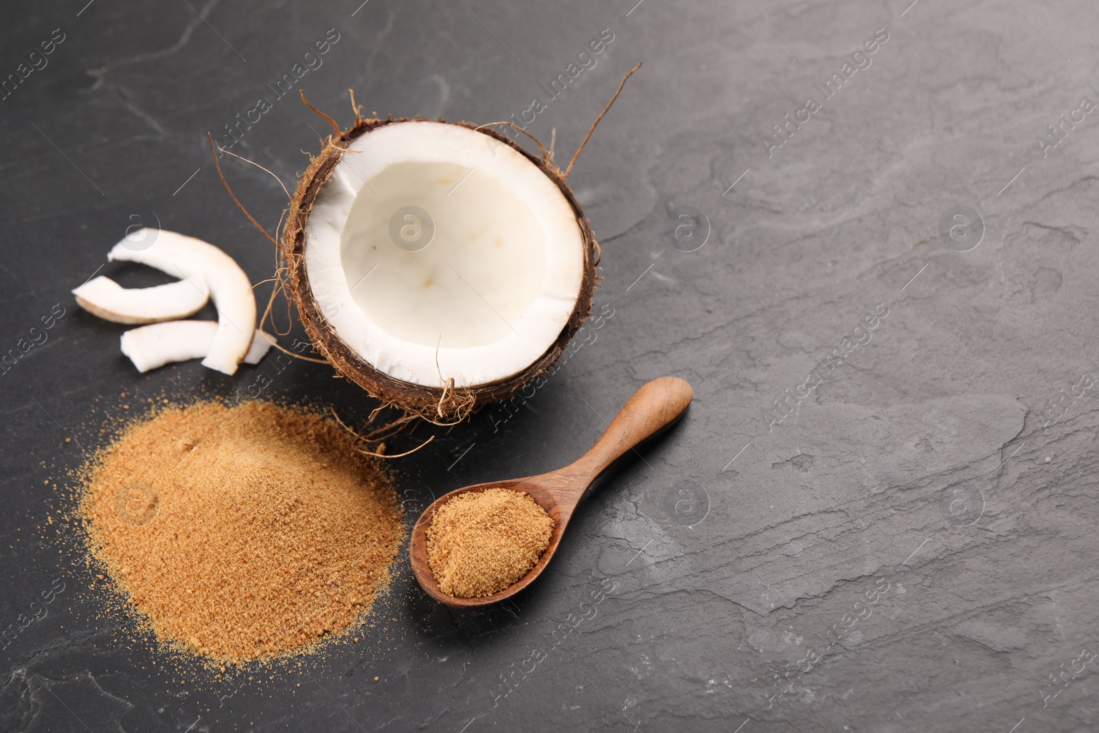 Photo of Coconut sugar, spoon and fruit on dark textured table, above view. Space for text