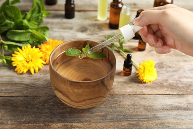 Photo of Woman dripping essential oil into bowl with water and mint on table