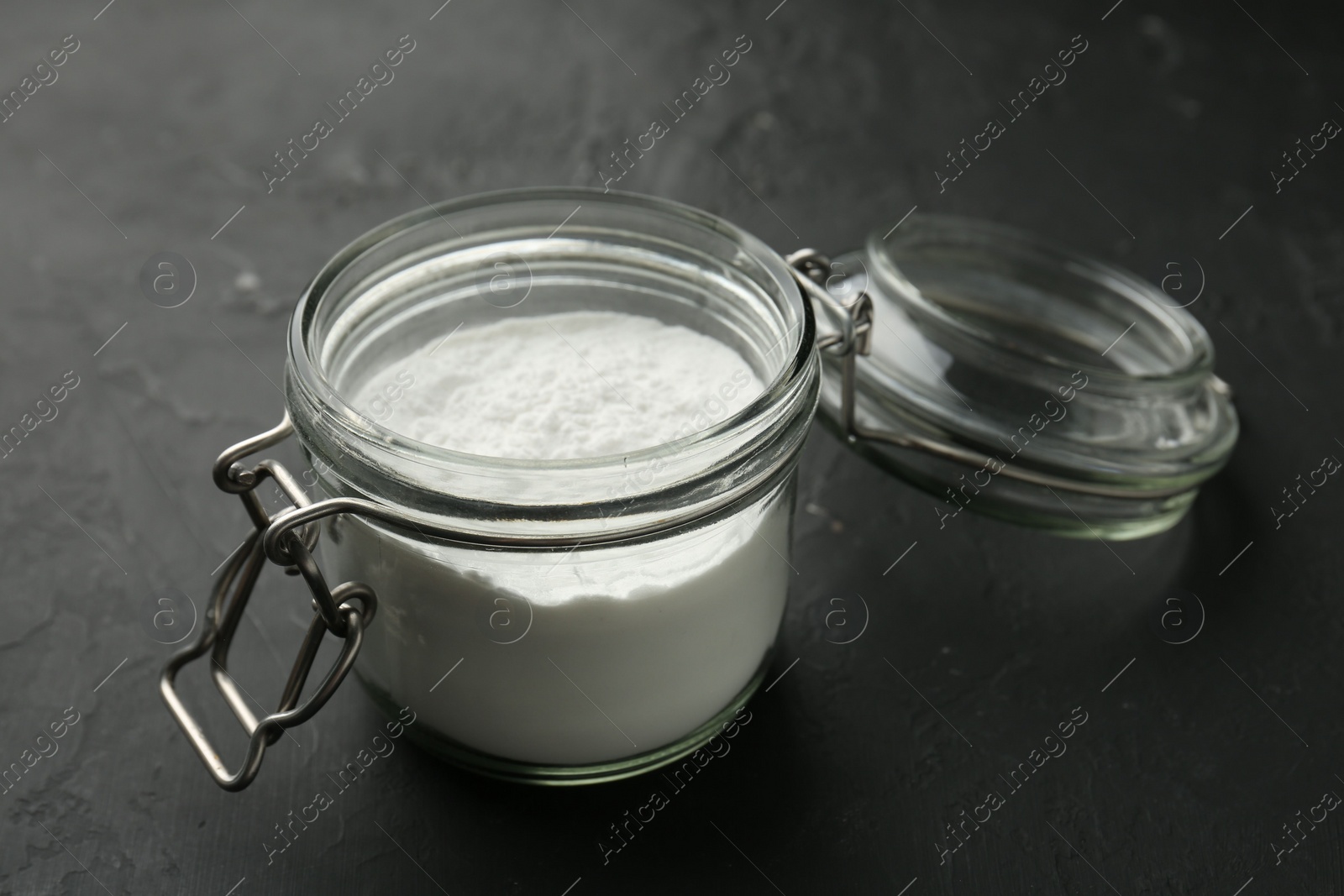 Photo of Baking powder in jar on black textured table, closeup