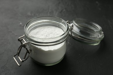 Baking powder in jar on black textured table, closeup