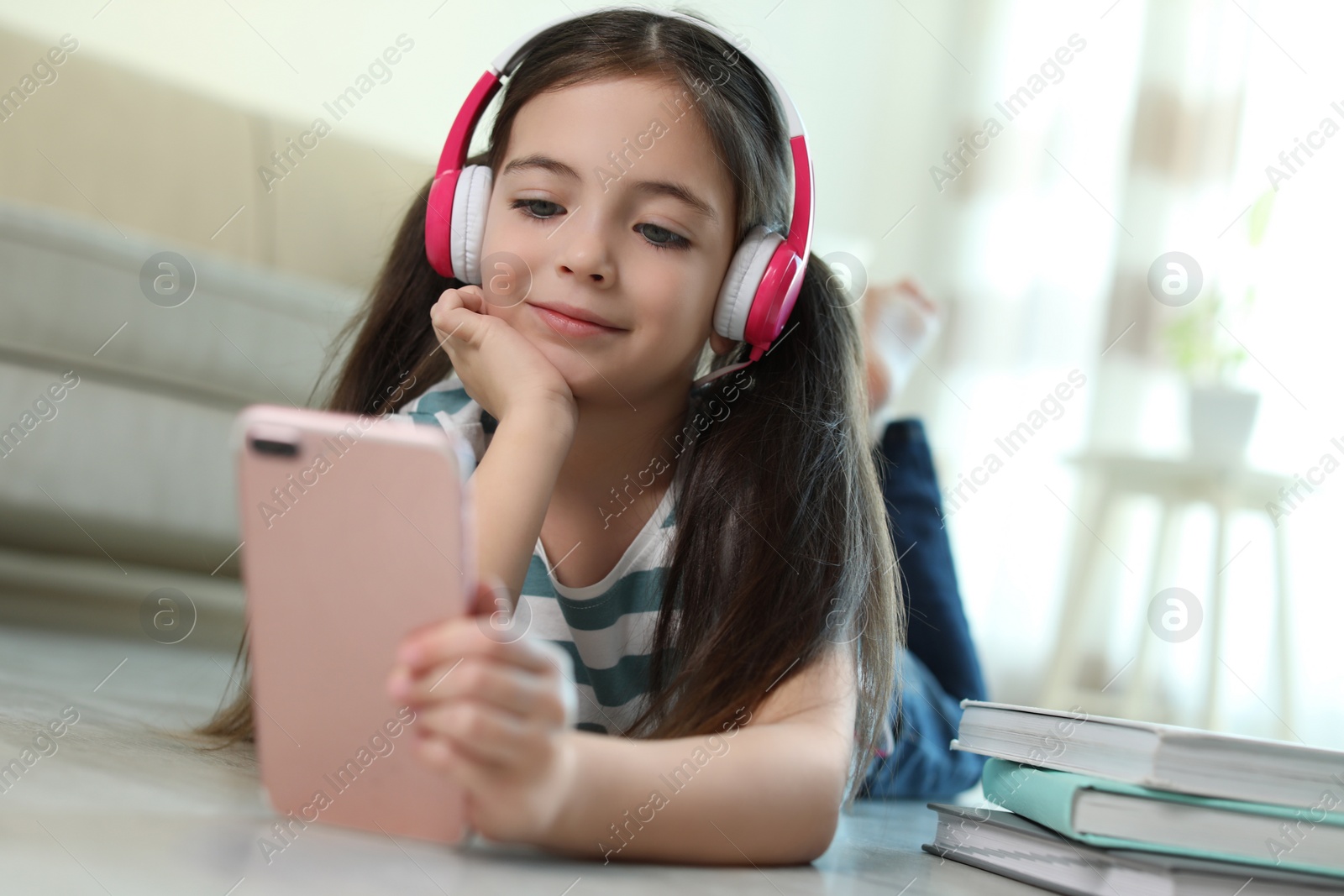 Photo of Cute little girl with headphones and smartphone listening to audiobook at home