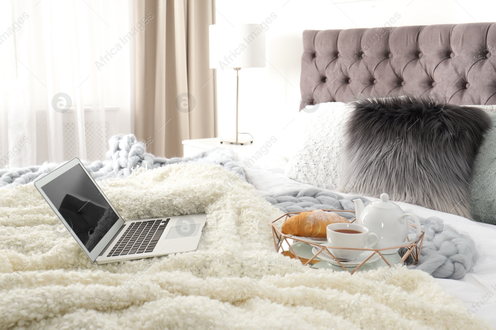 Photo of Tray with tasty breakfast and laptop on bed