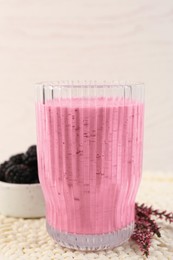 Photo of Glass of delicious blackberry smoothie, fresh berries and flowers on white wooden background