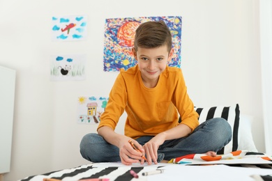 Photo of Little boy drawing picture on bed indoors