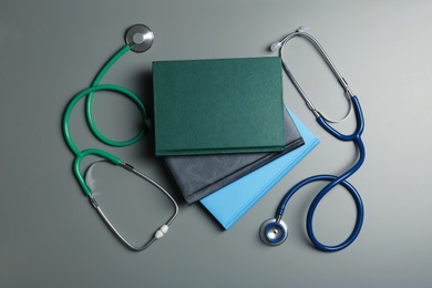 Student textbooks and stethoscopes on grey background, top view. Medical education