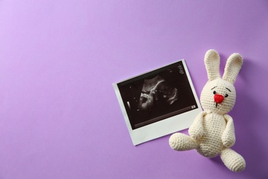 Ultrasound picture of baby and toy bunny on color background, top view with space for text