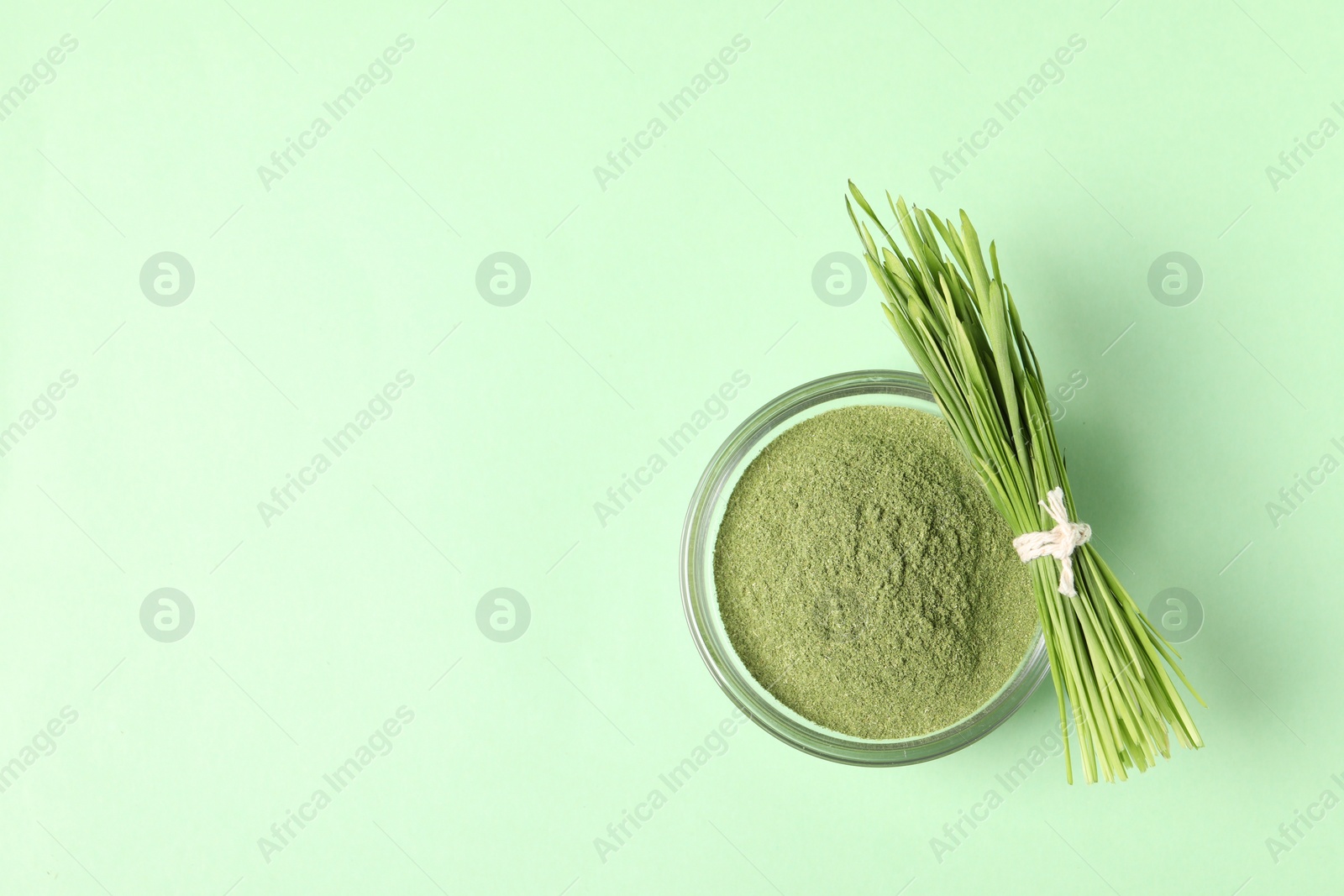 Photo of Wheat grass powder in bowl and fresh sprouts on green table, top view. Space for text