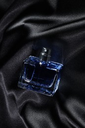 Photo of Luxury men's perfume in bottle on black satin fabric, above view