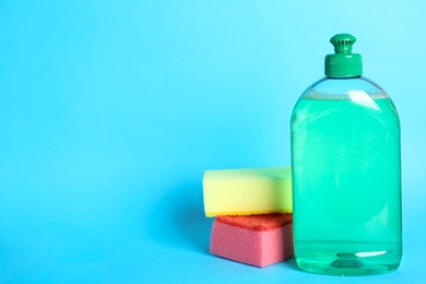 Photo of Detergent and sponges on light blue background, space for text