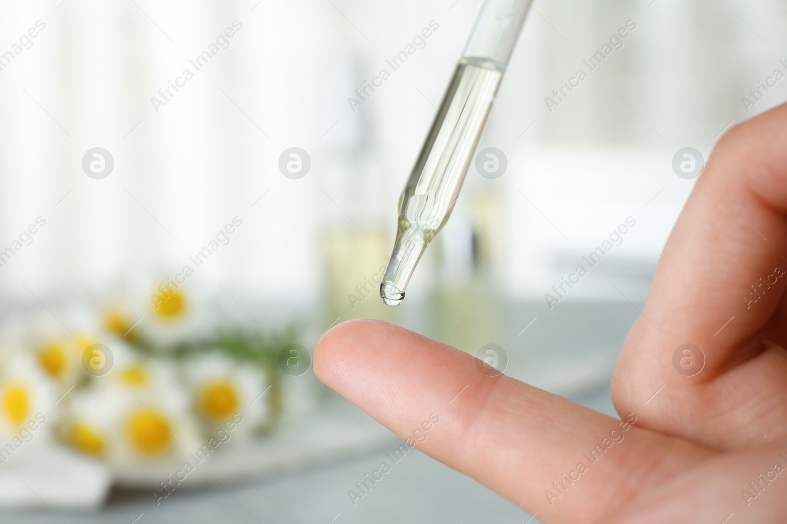 Photo of Woman dropping essential oil on finger over table, closeup