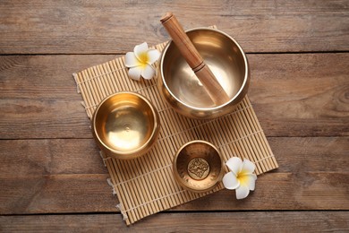 Golden singing bowls, mallet and flowers on wooden table, top view