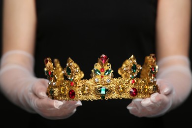 Photo of Woman holding luxurious crown on black background, closeup
