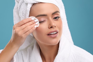 Photo of Beautiful woman removing makeup with cotton pad on light blue background