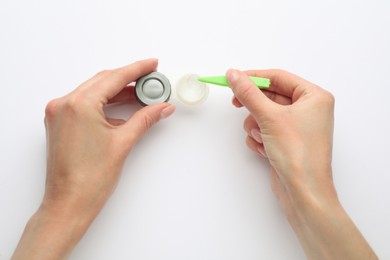 Woman taking contact lens from case with tweezers on white background, top view