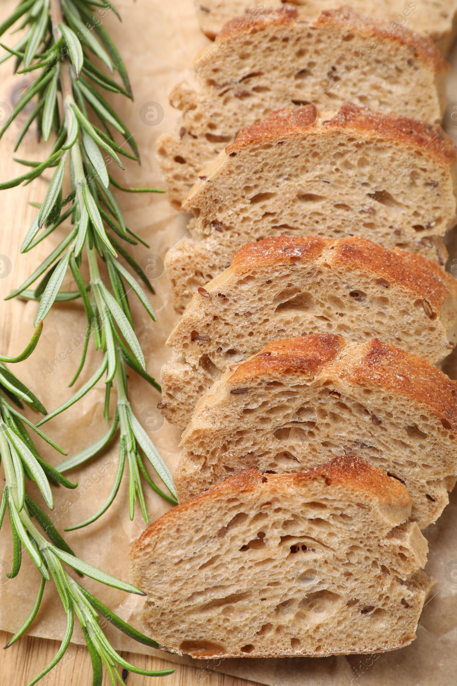 Photo of Cut buckwheat baguette with rosemary on wooden table, closeup