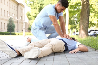 Passerby performing CPR on unconscious young man outdoors. First aid