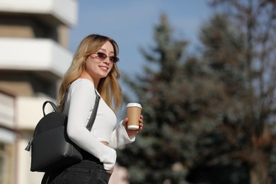 Photo of Young woman with stylish backpack and hot drink on autumn day, space for text