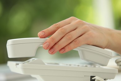 Assistant taking telephone handset on blurred background, closeup