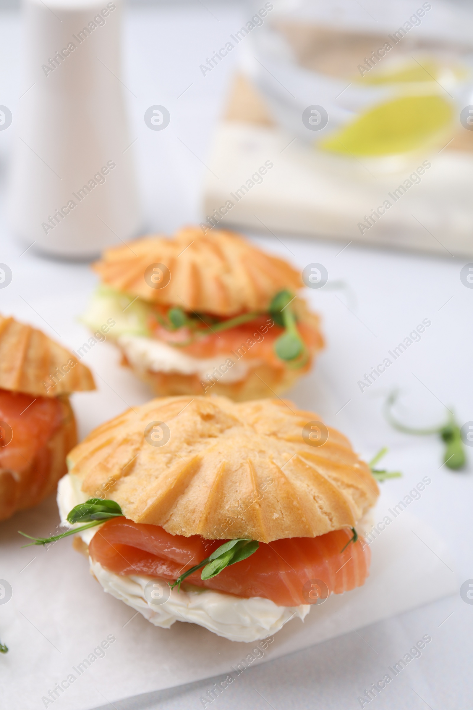 Photo of Delicious profiteroles with cream cheese and salmon on white table, closeup