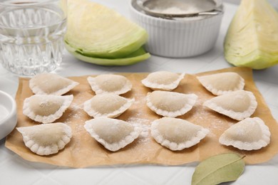 Photo of Raw dumplings (varenyky) with tasty filling and flour on white tiled table, closeup
