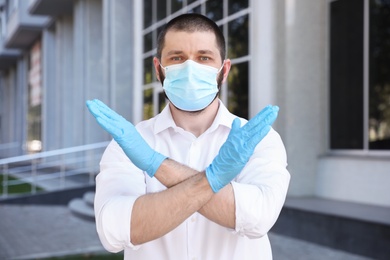 Man in protective face mask showing stop gesture outdoors. Prevent spreading of coronavirus