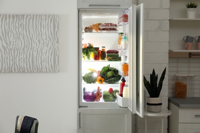 Open refrigerator full of products in stylish kitchen interior