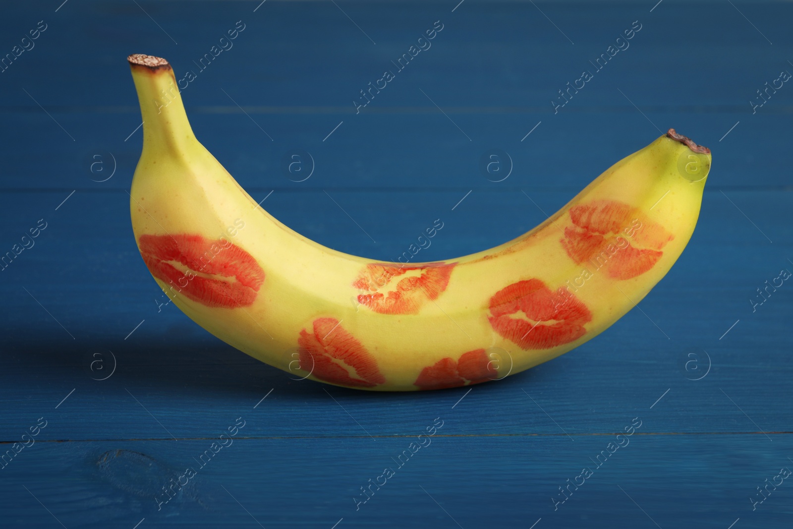 Photo of Banana covered with red lipstick marks on blue wooden table. Potency concept