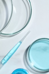 Photo of Pipette and petri dishes with liquid on white marble table, flat lay