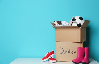 Photo of Donation boxes with toys and shoes on table against color background. Space for text