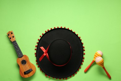 Photo of Mexican sombrero hat, maracas and guitar on green background, flat lay