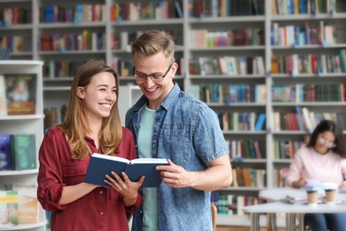 Photo of Happy young people with book in library. Space for text