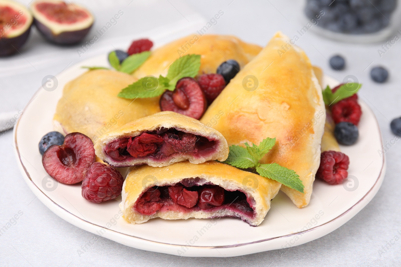 Photo of Plate of delicious samosas, berries and mint leaves on white table, closeup