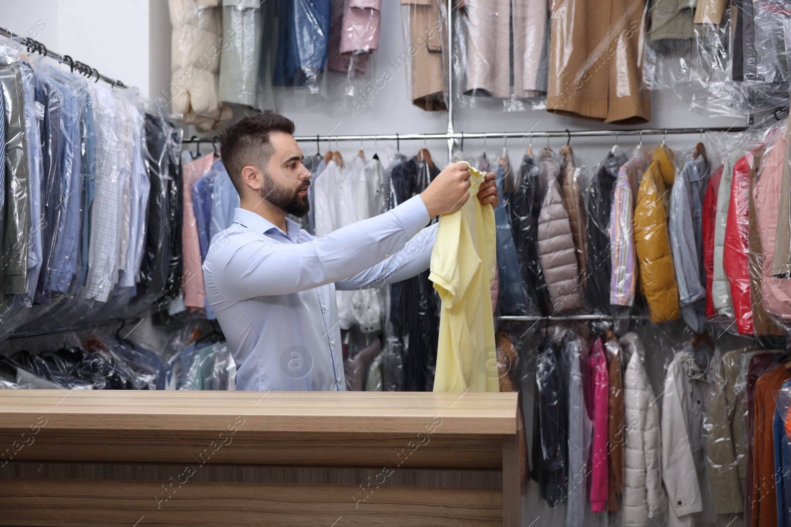 Photo of Dry-cleaning service. Worker holding t-shirt at counter indoors