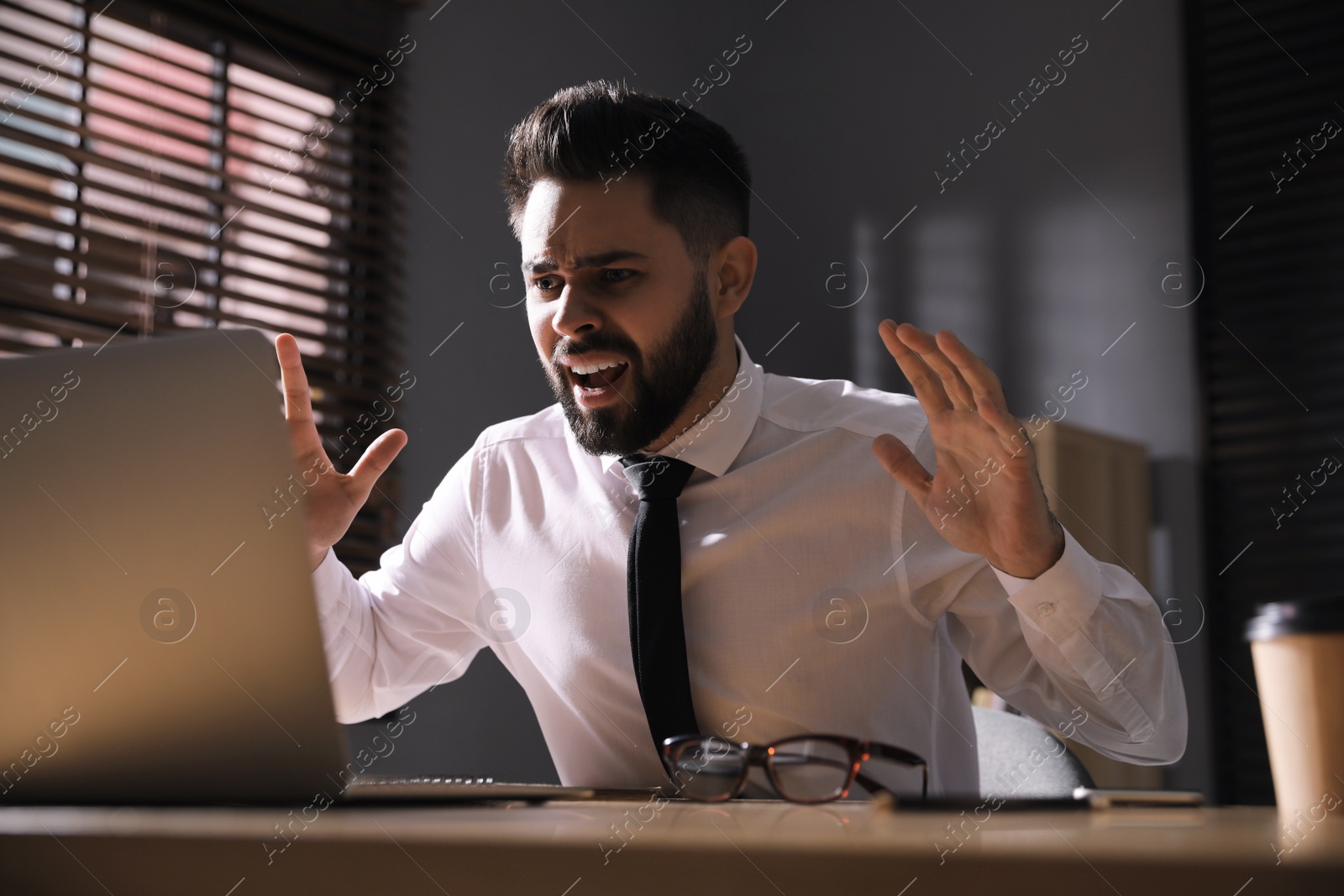 Photo of Emotional young businessman working on laptop in office. Online hate concept