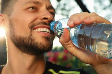 Photo of Happy man drinking water outdoors on hot summer day, closeup. Refreshing drink